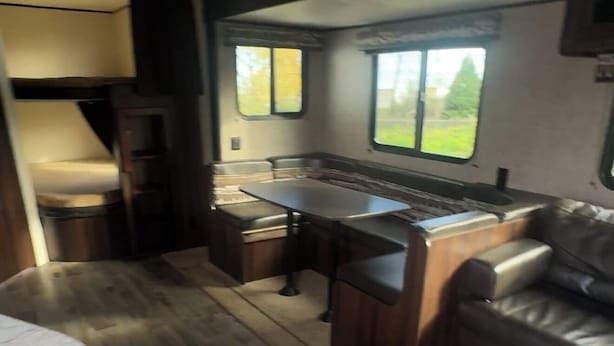 A compact RV kitchen with a marble countertop, wooden flooring, and a built-in seating area with a couch and table. - 3-bedroom CLEAN RV in perfect Maple Ridge with AC (Maple Ridge)