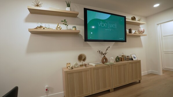 A modern living room with a mounted TV, wooden shelves with decorative items, a wooden cabinet, and a door.