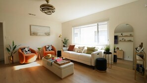 A spacious living room with a sofa, armchairs, a coffee table, and a large window.