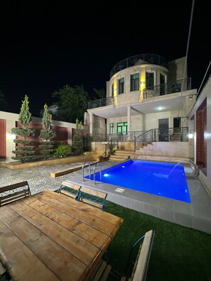 A pool with a wooden deck and a table, surrounded by potted plants and a building with a balcony. - Spacious 7-bedroom house in serene Baku with AC (Baku)