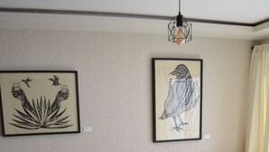 Una stanza con un divano in legno con cuscini gialli, una sedia in legno, un tavolino con un cappello e due opere d'arte appese al muro.