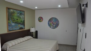 Una stanza con un letto, un quadro, due decorazioni a parete, una lampada e un televisore.