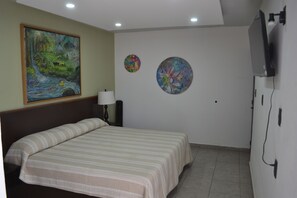 A room with a bed, a painting, two wall decorations, a lamp, and a TV. - Renovated 5 Element house with small pool 15 minutes from downtown Oaxaca (Oaxaca de Juárez)