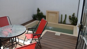 Un patio in legno con tavolo in vetro e sedie rosse, una piccola piscina e piante in vaso.