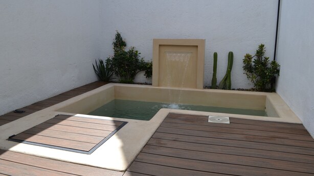 Una piccola vasca idromassaggio privata con un pontile in legno, circondata da piante e un muro.
