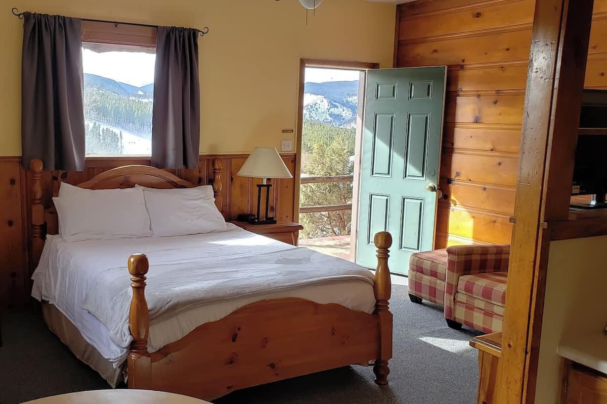 A wooden bed in a room with a view of mountains through a window.