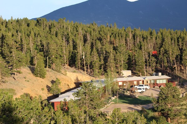 A residential area with a house, a car, and a forested hillside. - Sundance Lodge (Nederland)