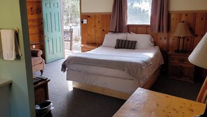 Un dormitorio con cama, mesita de noche, lámpara, ventana con cortinas y puerta que da al exterior.