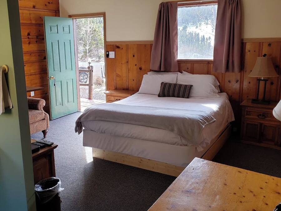 A bedroom with a bed, a nightstand, a lamp, a window with curtains, and a door leading outside.