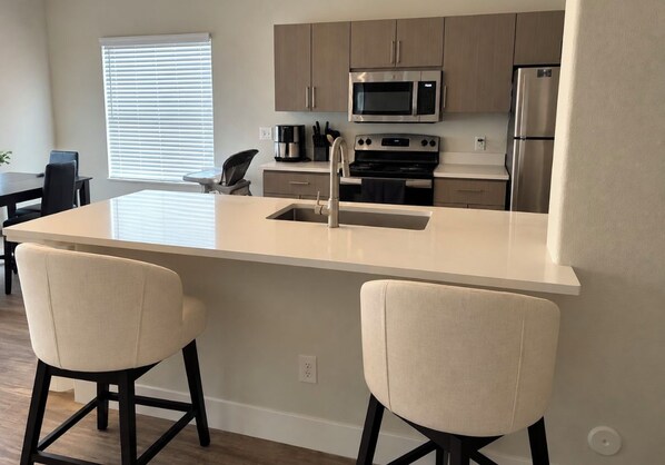 A modern kitchen with a central island, stainless steel appliances, and two bar stools. - Cozy 2-bedroom apartment with AC in soothing Glendale (Glendale)