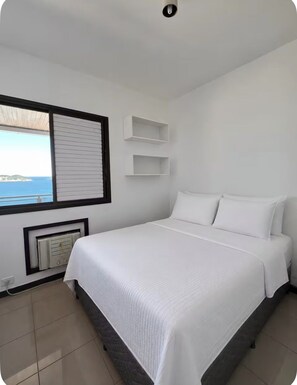 Ein Schlafzimmer mit Bett, einem Fenster mit Jalousien, einer eingebauten Ablage und Meerblick.