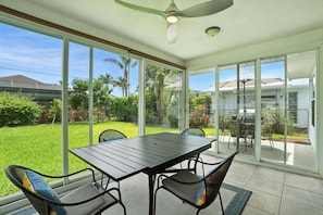 Eine überdachte Terrasse mit Tisch, Stühlen, großen Glasüren und einem Deckenventilator.