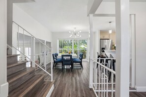 A modern interior with a staircase, a dining area with blue chairs, and a kitchen in the background.