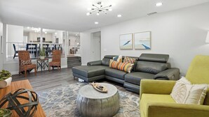 En moderne stue med en grå hjørnesofa, en gul lænestol og et spiseområde med fletstole.