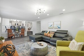 A modern living room with a grey sectional sofa, a yellow armchair, and a dining area with wicker chairs.