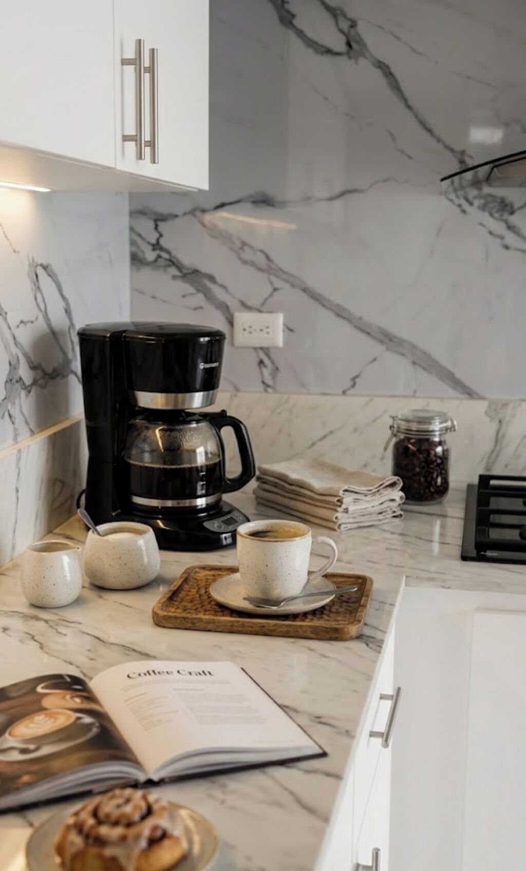 Une cuisine équipée d’une machine à café, de tasses, d’un livre et d’un bocal de grains de café.