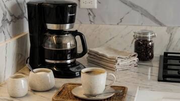 A kitchen with a coffee maker, cups, a book, and a jar of coffee beans.
