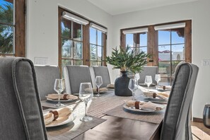 A dining area with a table set for four, featuring a vase with greenery, clear glassware, and neatly folded napkins. - The Villa at Fountain Hills | Pool, Hot Tub, Game Room, Ping Pong & Sleeps 20 (Fountain Hills)