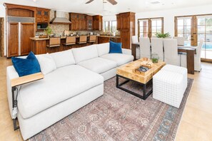 A modern living room with a sectional sofa, a coffee table, and a dining area with a pool view. - The Villa at Fountain Hills | Pool, Hot Tub, Game Room, Ping Pong & Sleeps 20 (Fountain Hills)