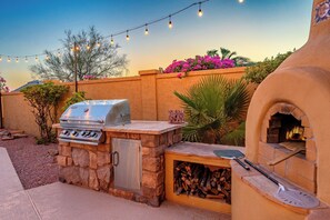 An outdoor barbecue area with a stone grill, a pizza oven, and a string of lights. - The Villa at Fountain Hills | Pool, Hot Tub, Game Room, Ping Pong & Sleeps 20 (Fountain Hills)