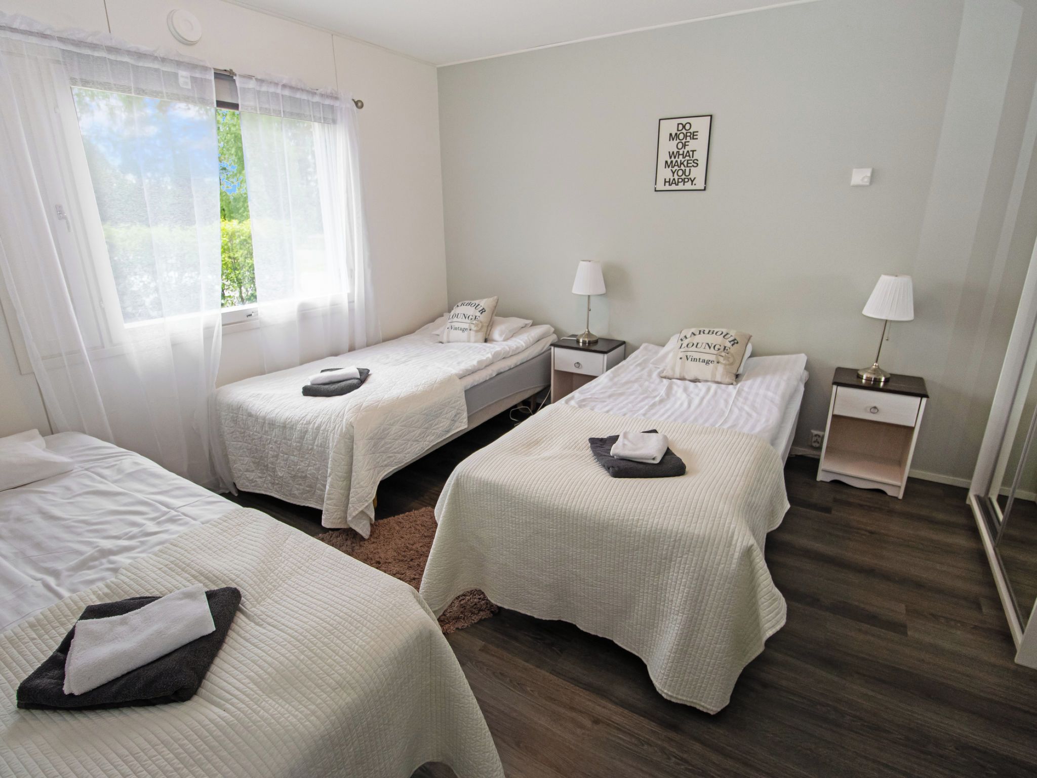 A hotel room with three beds, a window with sheer curtains, a wall-mounted sign, and a wooden floor.