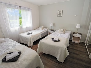 Habitación de hotel con tres camas, una ventana con cortinas traslúcidas, un letrero en la pared y suelo de madera.