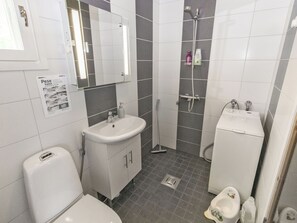 A bathroom with a toilet, sink, mirror, shower, and a small cabinet.