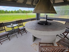 A covered outdoor seating area with a round table and chairs, a grill, and a view of a green field. - Apartment Tupa by Interhome (Juva)