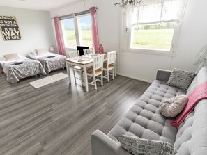 A modern living room with a grey sofa, a dining table with chairs, two beds with star-patterned bedding, and large windows with curtains. - Vacation home Tupa by Interhome (Juva)