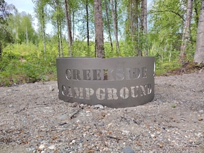 A metal sign with the text 'CREEKSIDE CAMPING GROUNDS' on a gravel surface.