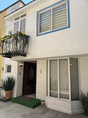 Ein zweistöckiges Haus mit Balkon, Eingangstür und einem Fenster mit Rollläden.