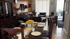 Een eethoek met een houten tafel voor vier personen, stoelen, een bank en een potplant.