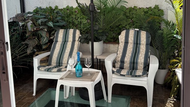 Een terras met twee witte stoelen, een tafel, een witte parasol en potplanten.