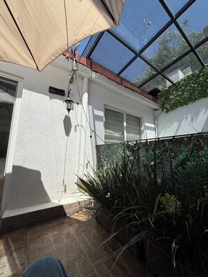 Eine sonnige Terrasse mit Glasveranda, Blumentöpfen und einer weißen Wand mit Fenster.