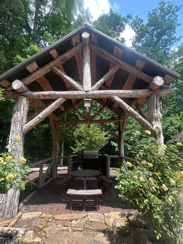 A rustic wooden gazebo with a grill and a table.