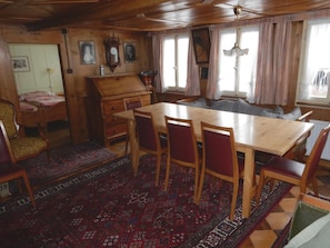 Ein traditioneller Essraum mit einem großen Tisch, Stühlen, einem Klavier und einem gemusterten Teppich.