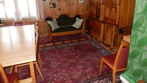 Une pièce comprenant un canapé en bois, une table à manger, des chaises, un tapis à motifs et des meubles de rangement en bois.
