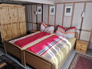 Ein hölzernes Bett mit gemustertem Überwurf, ein Nachttisch, ein Holzschrank und eine Wand mit gerahmten Bildern.