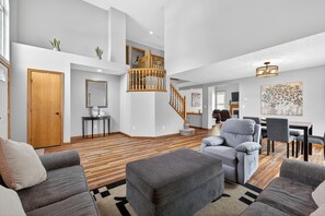 A spacious living area with a wooden staircase, grey sofas, and a dining table.