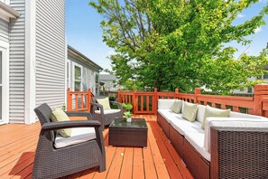 A deck with wicker furniture, a white railing, and a large tree.