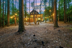 Eine Hütte im Wald mit Lichterketten, Holzstühlen und freiem Blick auf die umliegenden Bäume.
