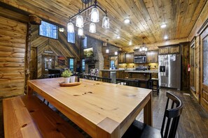 Interior d'una cabana rústica amb taula de dinar de fusta, llar de pedra i zona de cuina amb electrodomèstics moderns.