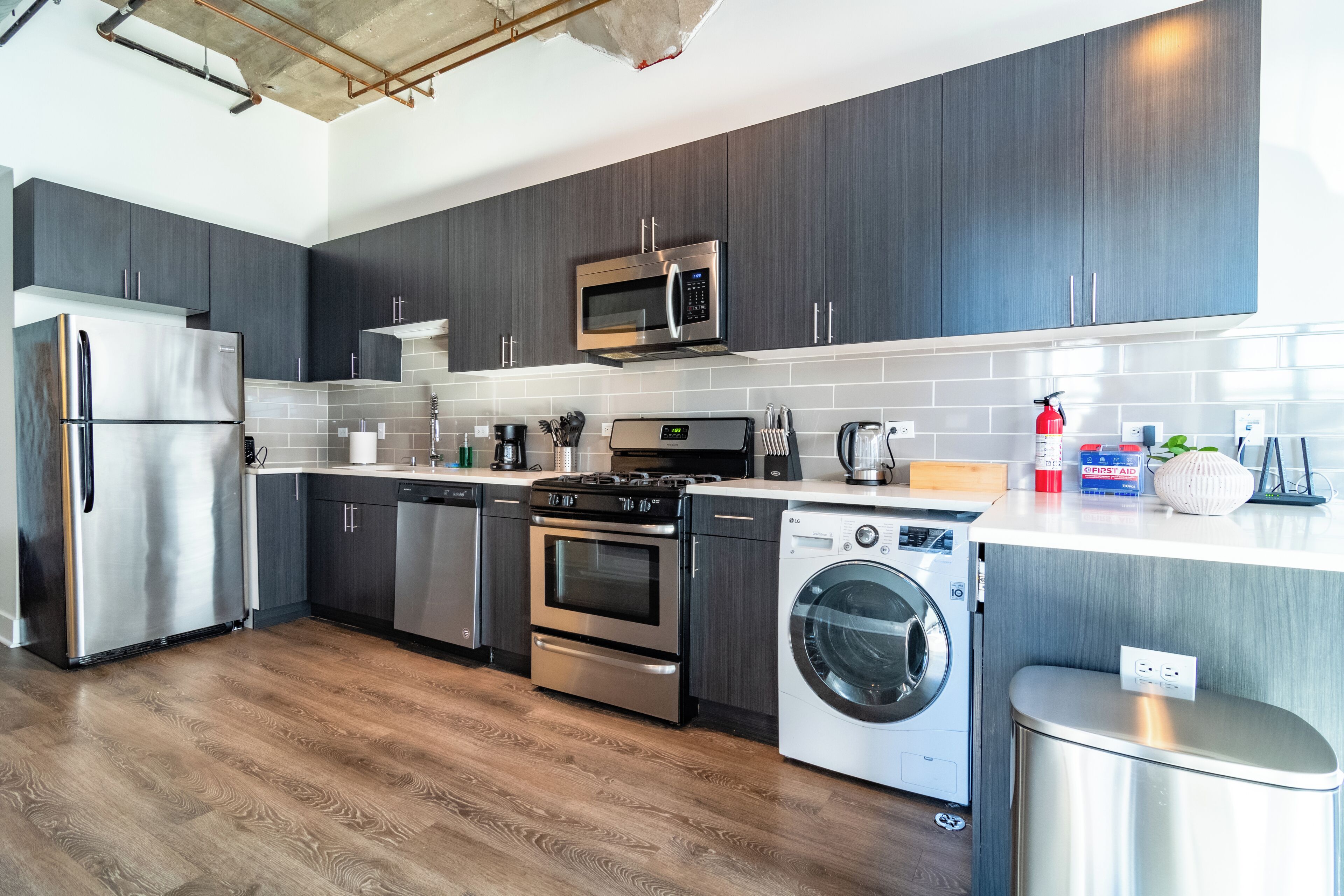 A modern kitchen with dark cabinets, stainless appliances, and a wooden floor.