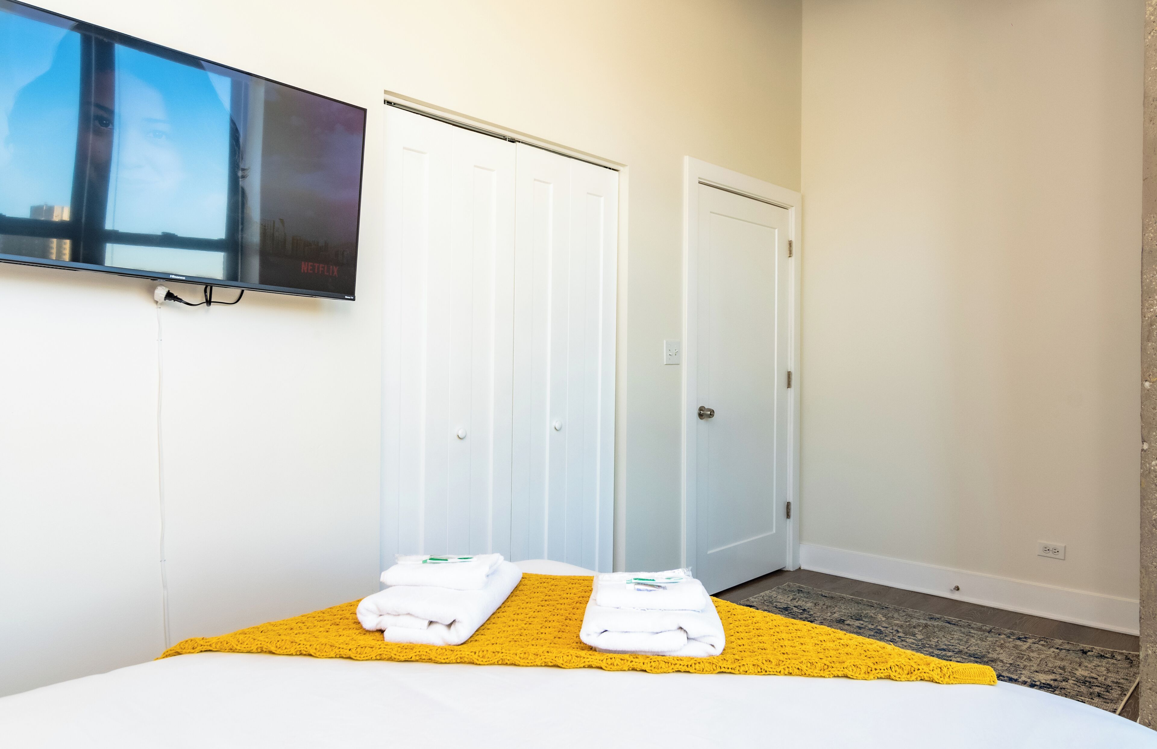 A hotel room with a bed, a TV mounted on the wall, and a set of white doors.