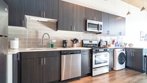 A modern kitchen with dark cabinets, stainless steel appliances, and a tiled backsplash. - Spacious 3BR Suite with Skyline Views Near McCormick (Chicago)