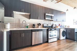 A modern kitchen with dark cabinets, stainless steel appliances, and a tiled backsplash. - Spacious 3BR Suite with Skyline Views Near McCormick (Chicago)