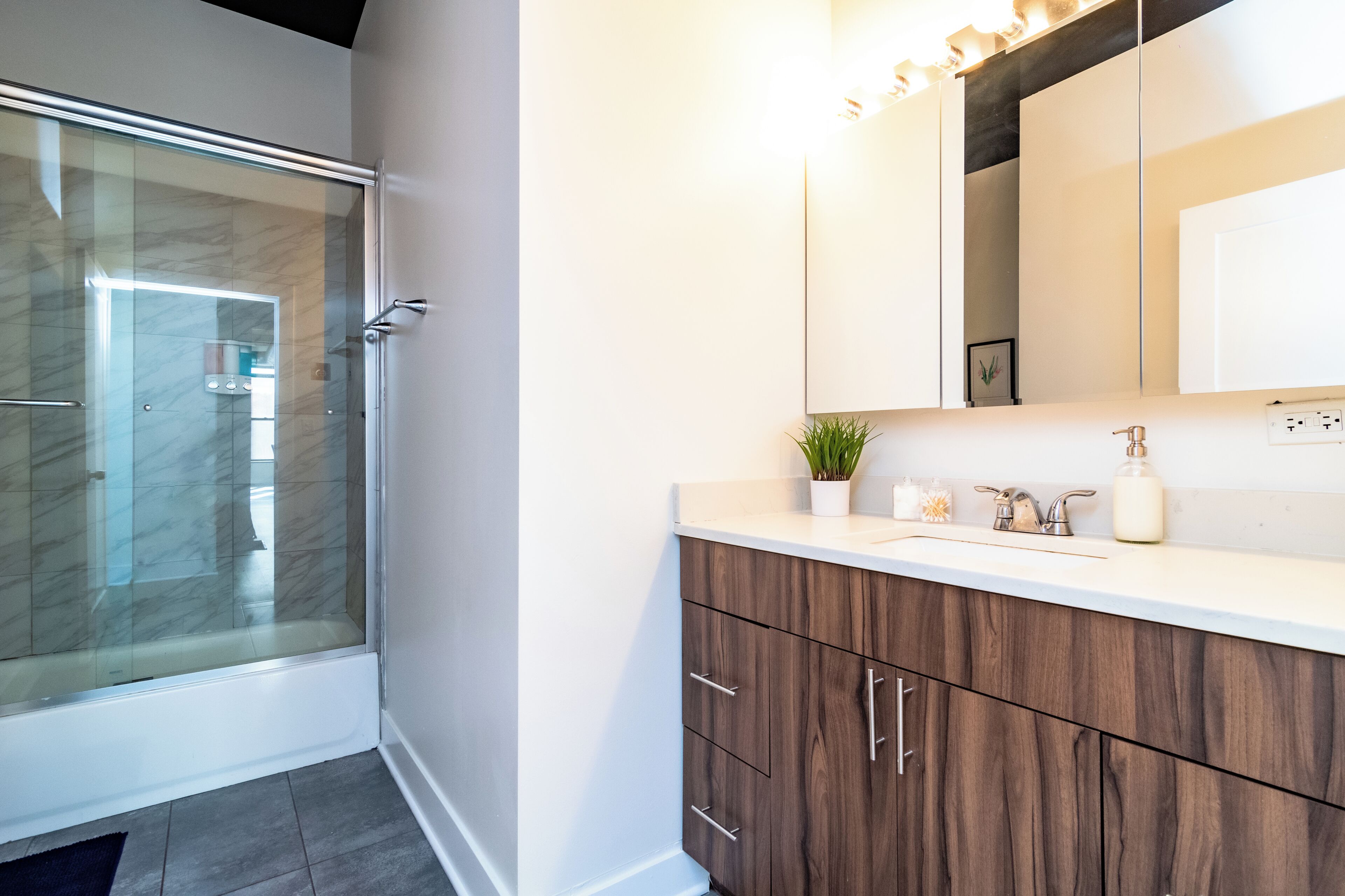 Une salle de bain moderne avec une douche à parois de verre, un meuble-lavabo blanc avec un miroir et des armoires en bois.