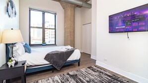 A bedroom with a bed, a nightstand, a lamp, a TV, and a window. - Spacious 3BR Suite with Skyline Views Near McCormick (Chicago)