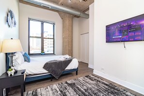 A bedroom with a bed, a nightstand, a lamp, a TV, and a window. - Spacious 3BR Suite with Skyline Views Near McCormick (Chicago)