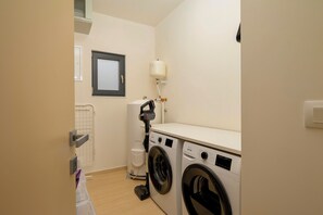 A laundry room with a front-loading washing machine, a stacked washer and dryer, a vacuum cleaner, and a water tank. - Villa Uno (Istria - Žminj) (Rovinj)